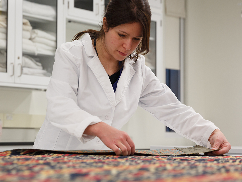 A brunette woman in a lab coat inspects a colorful textile.