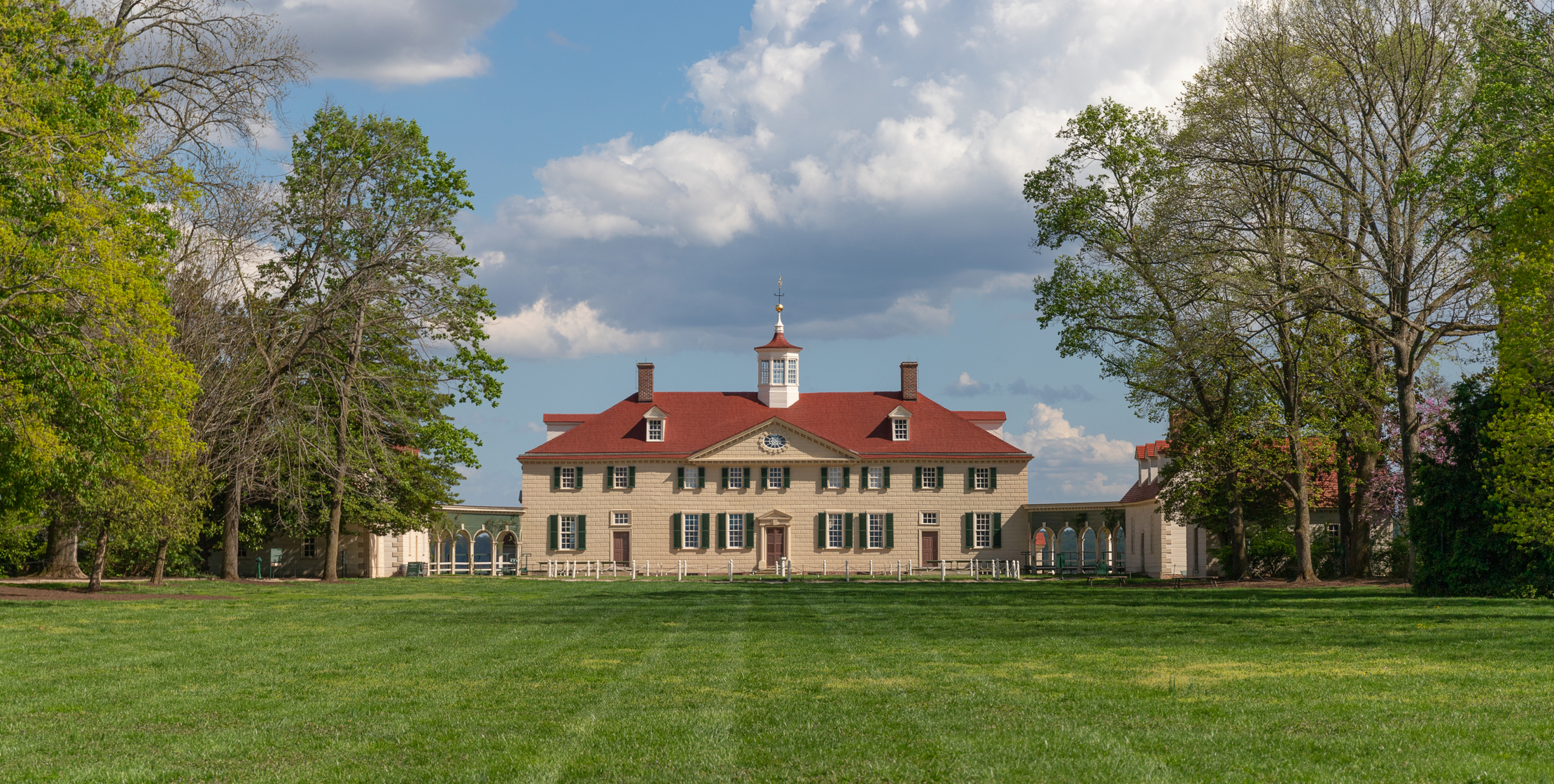 Large house at the far end of a green lawn with a pale yellow façade and red roof