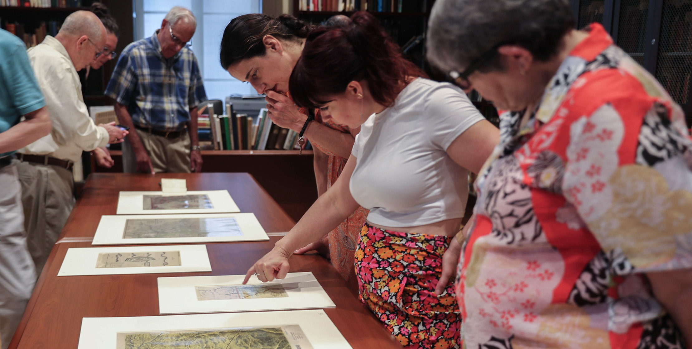 Three women examine a selection of maps laid flat on a table