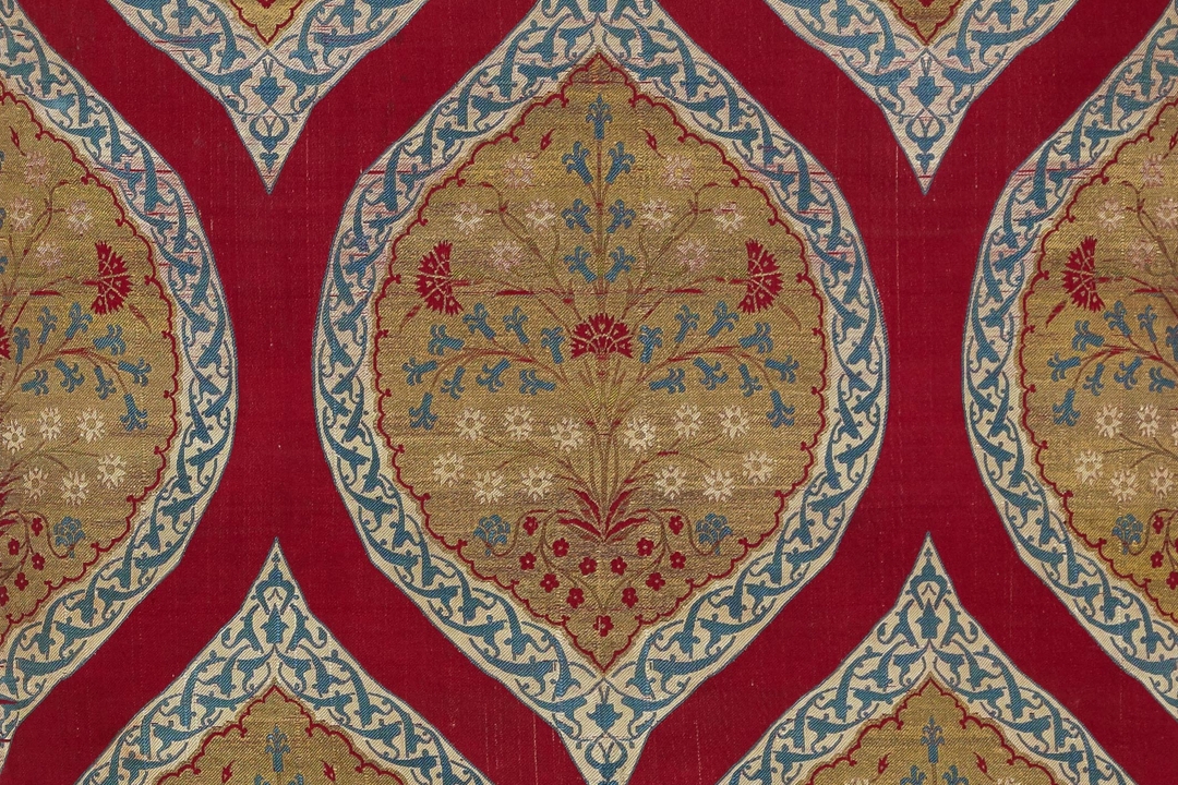 Detail of a textile depicting a bouquet of red, blue and white flowers on a gilt ground within a scalloped medallion with a whit