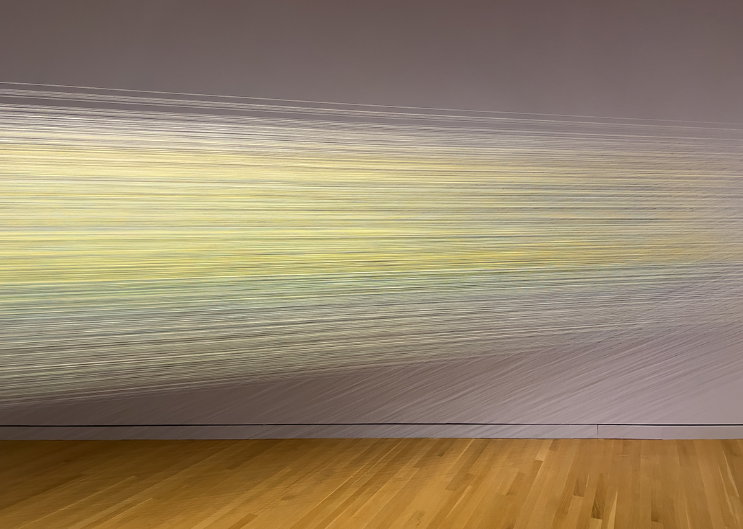 An art installation comprised of hundreds of multicolored threads stretched taut between two walls.