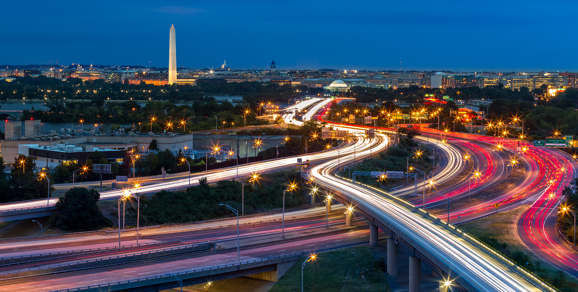 A view of highways at night, with the Washington Monument in the distance