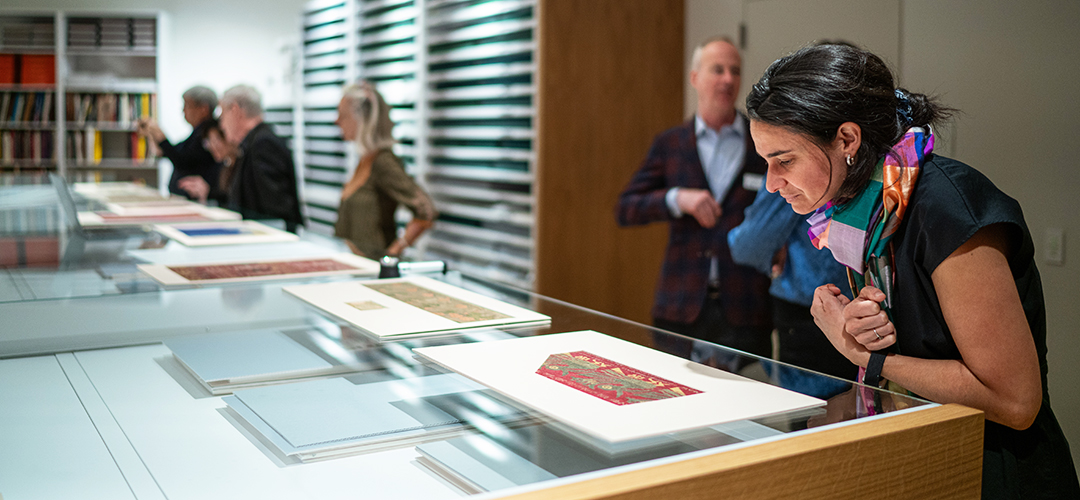 A scholar examines a textile fragment in a case as part of a group workshop