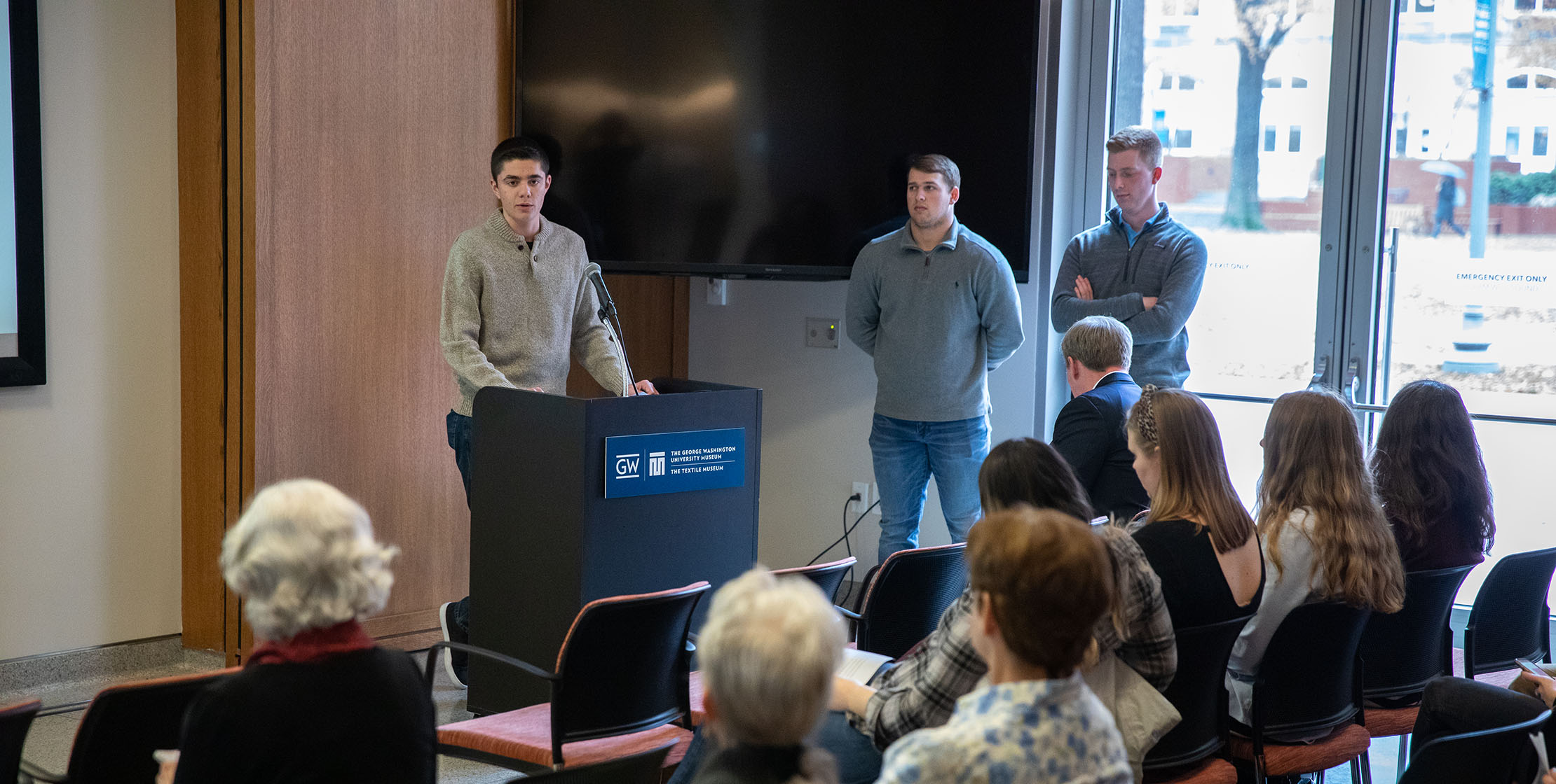 View of a person speaking at a podium in front of a room of people