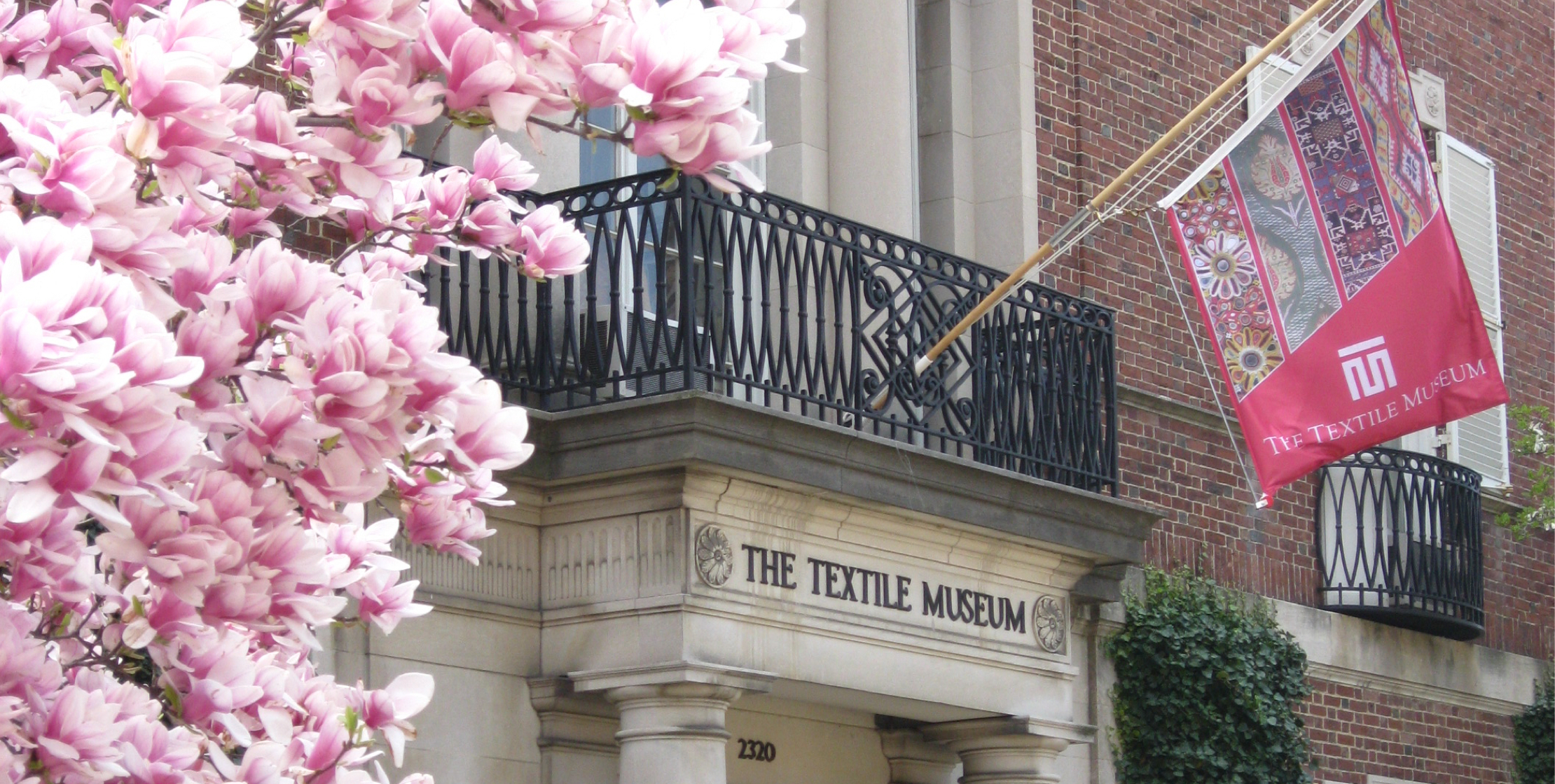 A balcony with a flag hanging from it, foregrounded by a cherry blossom tree. 