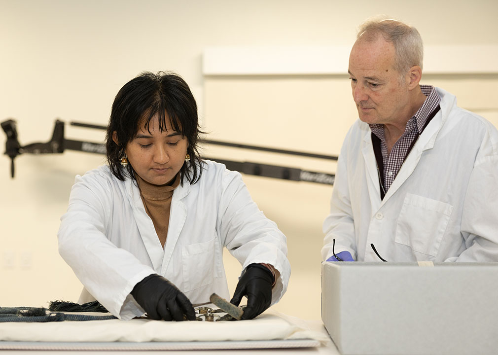 a man and a woman stand looking at objects in a conservation lab