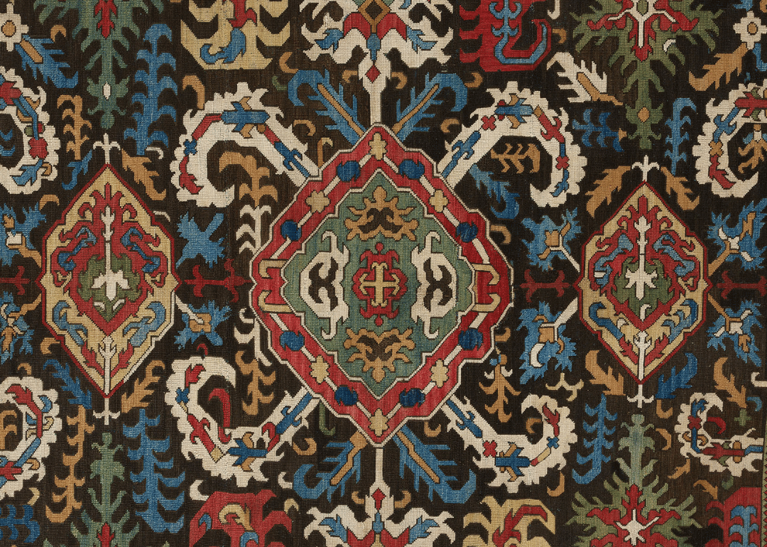 darkly colored rug with stylized floral designs in red, blue, white and green