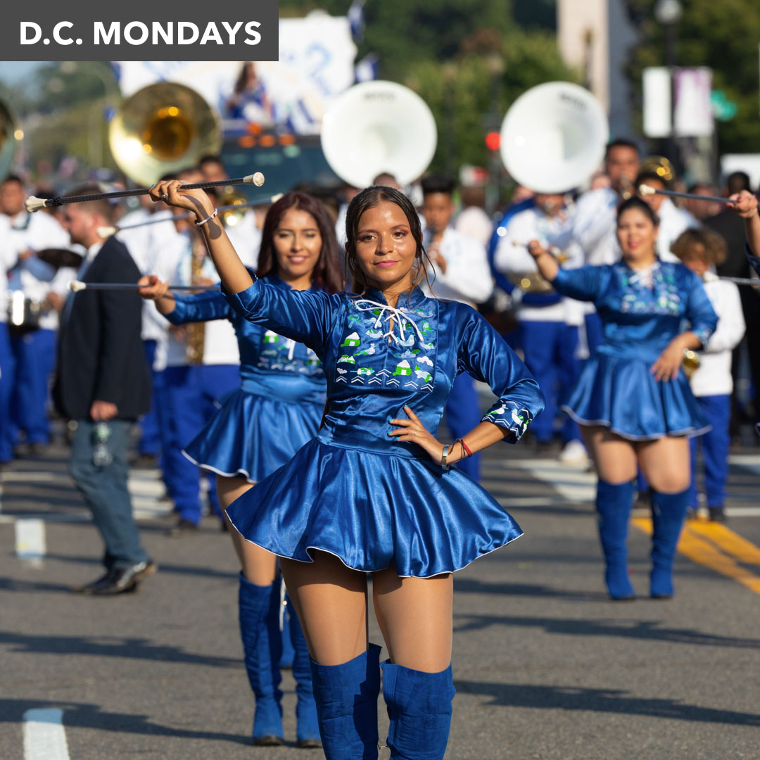 a parade of performers in blue outfits. The central girl is twirling a baton