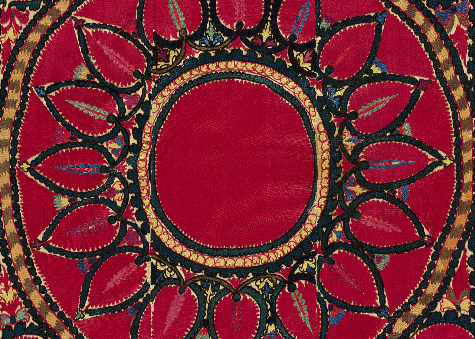 detail of a red textile with large central flower outlined in black and yellow