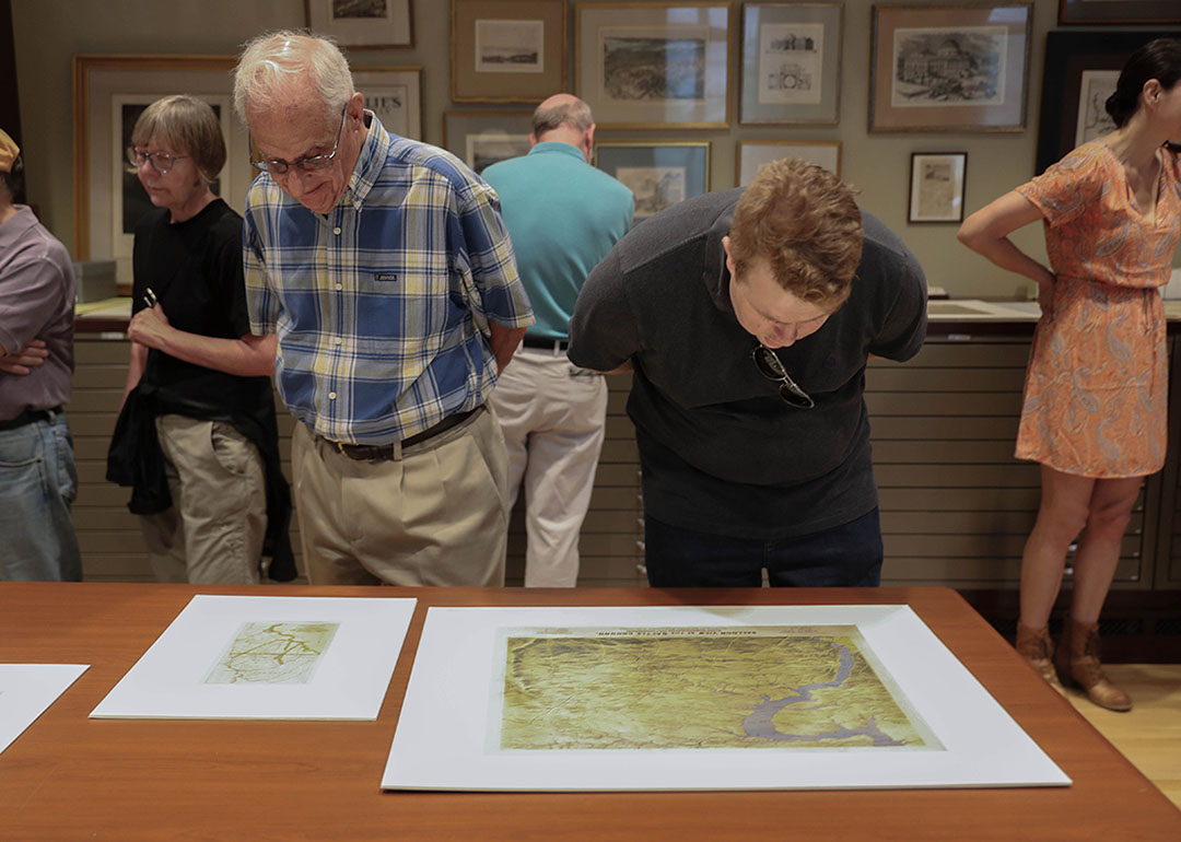 two men peer at maps on a table