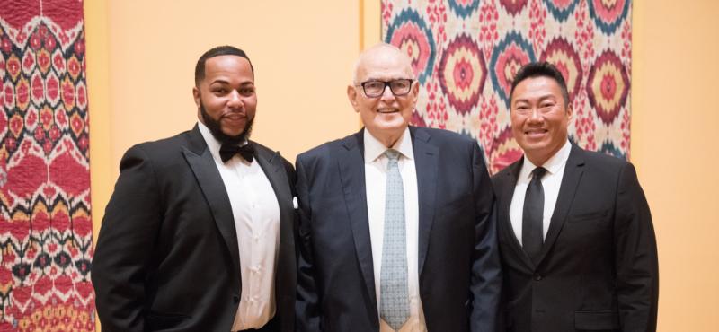 Three men smiling in front of a textile