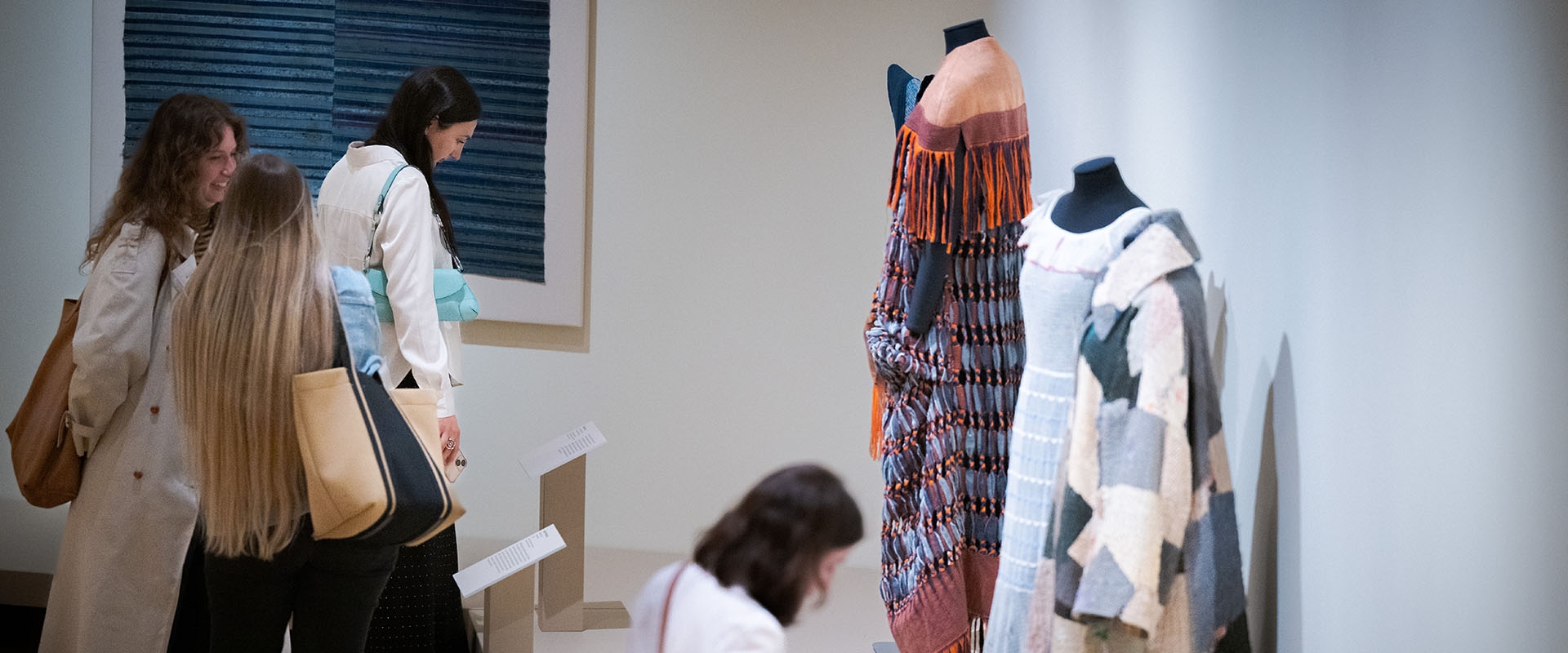visitors in a museum gallery look at the exhibition on display, featuring dress forms