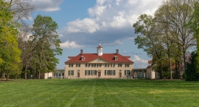 Large house at the far end of a green lawn with a pale yellow façade and red roof
