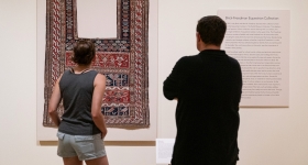 Two people look at an ornate horse cover on display in a museum