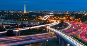 A view of highways at night, with the Washington Monument in the distance
