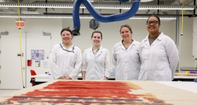 Four women in lab coats smile in a conservation lab