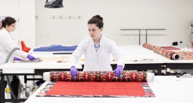 a woman in a white lab coat unfurls a large textile 