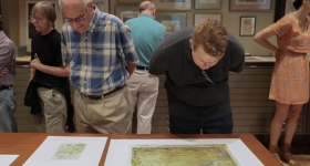 two men lean over to look at maps laid out on a table