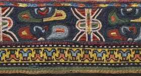 decorative textile border on a dark blue ground with abstracted shapes in blue, yellow, red and green