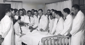 doctors in lab coats standing around a hospital bed