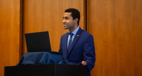 A young man stands behind a podium, presenting
